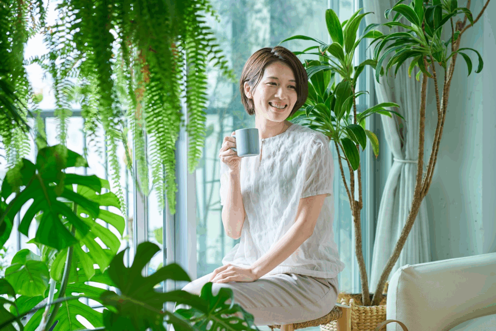 A woman smiling while holding a mug, surrounded by indoor plants :States of Mind