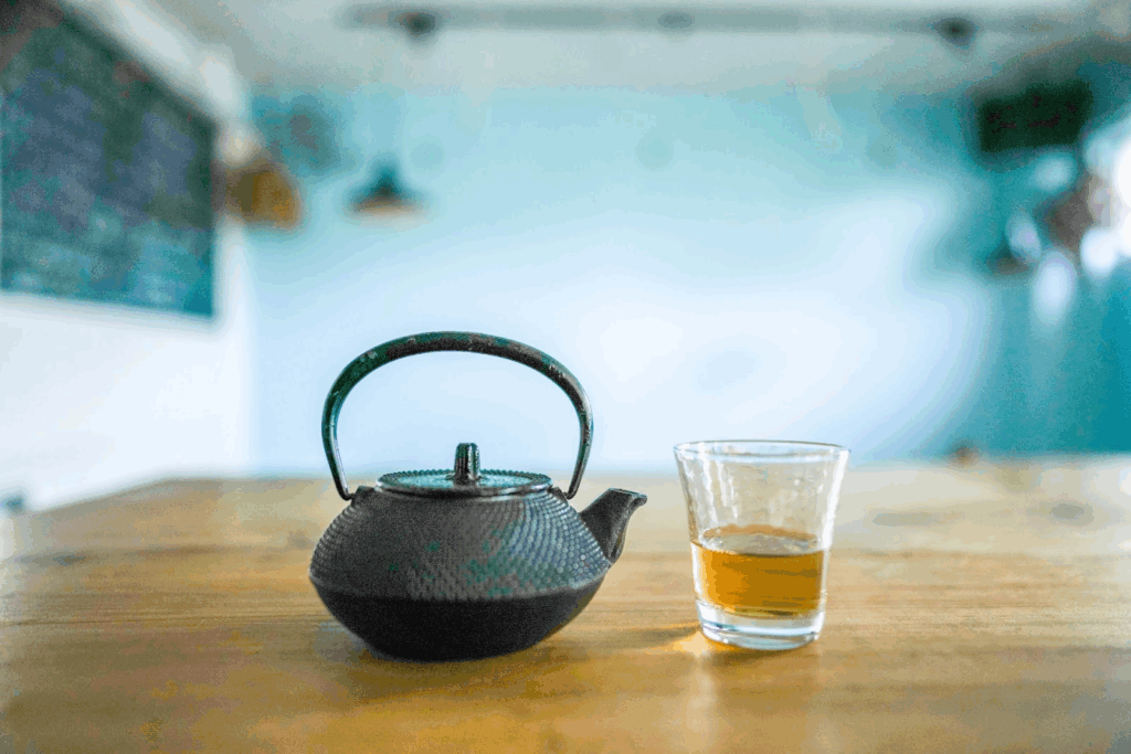 木のテーブルの上に置かれた鉄瓶と、半分ほどお茶が入ったガラスのコップ。背景は淡いブルーで落ち着いた雰囲気。：マインドフルネス