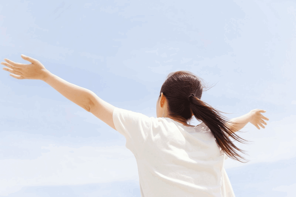 Self-compassion: A back view of a woman spreading her arms wide under the blue sky, feeling a sense of freedom.