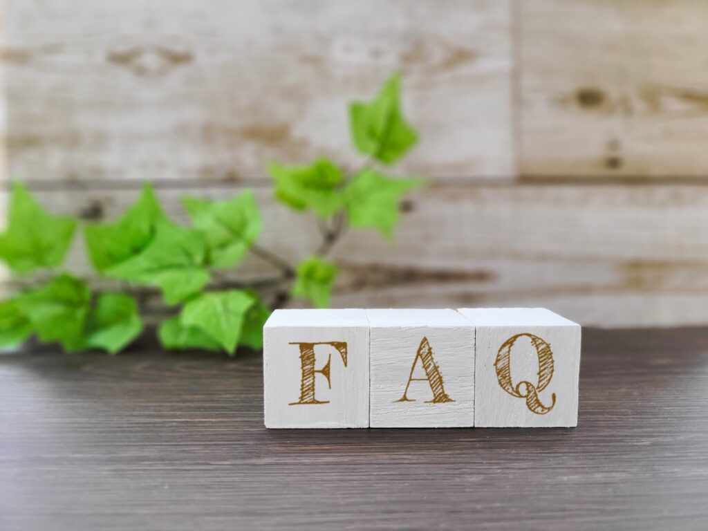 日本語:
木目の背景と緑の葉を背に、「FAQ」と書かれた白い木製ブロック:不安を和らげる瞑想