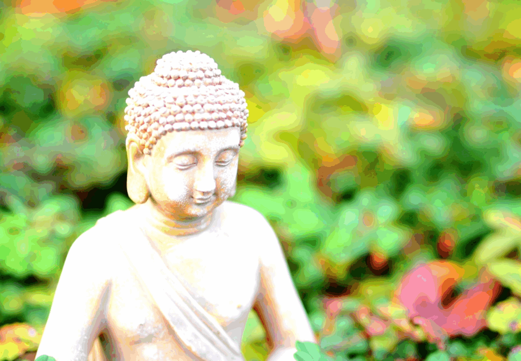 緑の草花に囲まれた、穏やかな表情を浮かべる仏像:セルフコンパッション