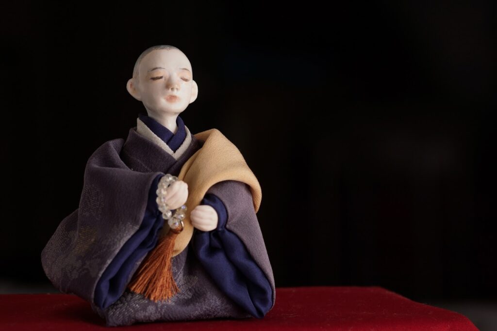 A figurine of a monk wearing traditional robes and holding prayer beads, depicted with a calm expression in meditation : Breathing Techniques for Anxiety