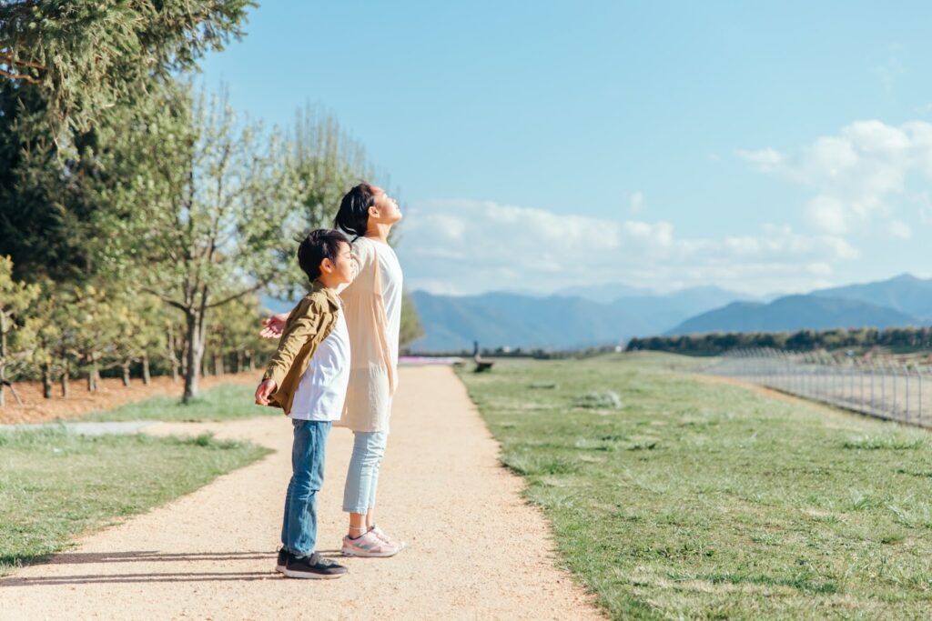 A parent and child standing on a path under the blue sky, taking a deep breath, surrounded by mountains and nature : Breathing Techniques for Anxiety