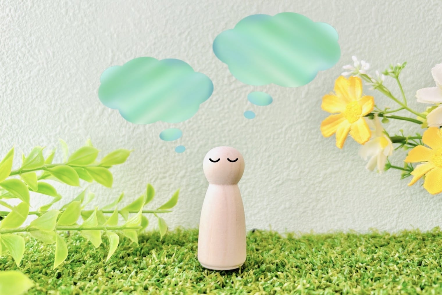 A small wooden figurine stands on green grass with closed eyes and a calm expression. Two light blue thought bubbles float above its head, surrounded by yellow flowers and green leaves. :Meditation for Stress and Anxiety