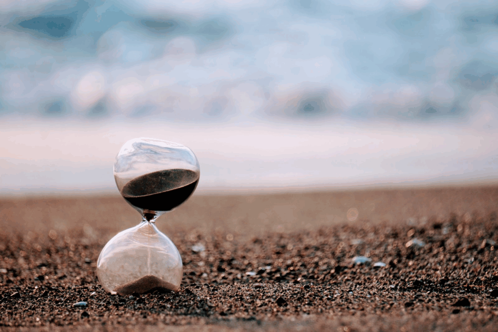 An hourglass placed on the sandy beach, with the shoreline and waves in the background : Meditation Timer