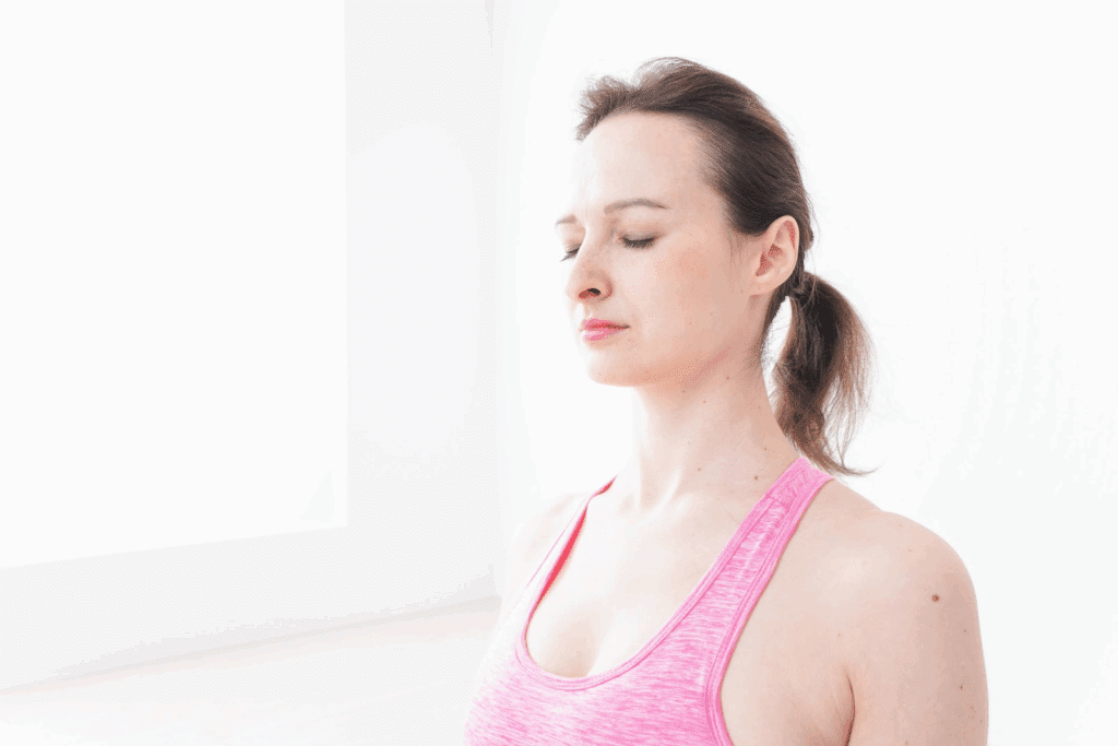 A woman in a bright white room meditates with her eyes closed. She is wearing a pink sports outfit and has a calm, peaceful expression.: Meditation for Stress and Anxiety