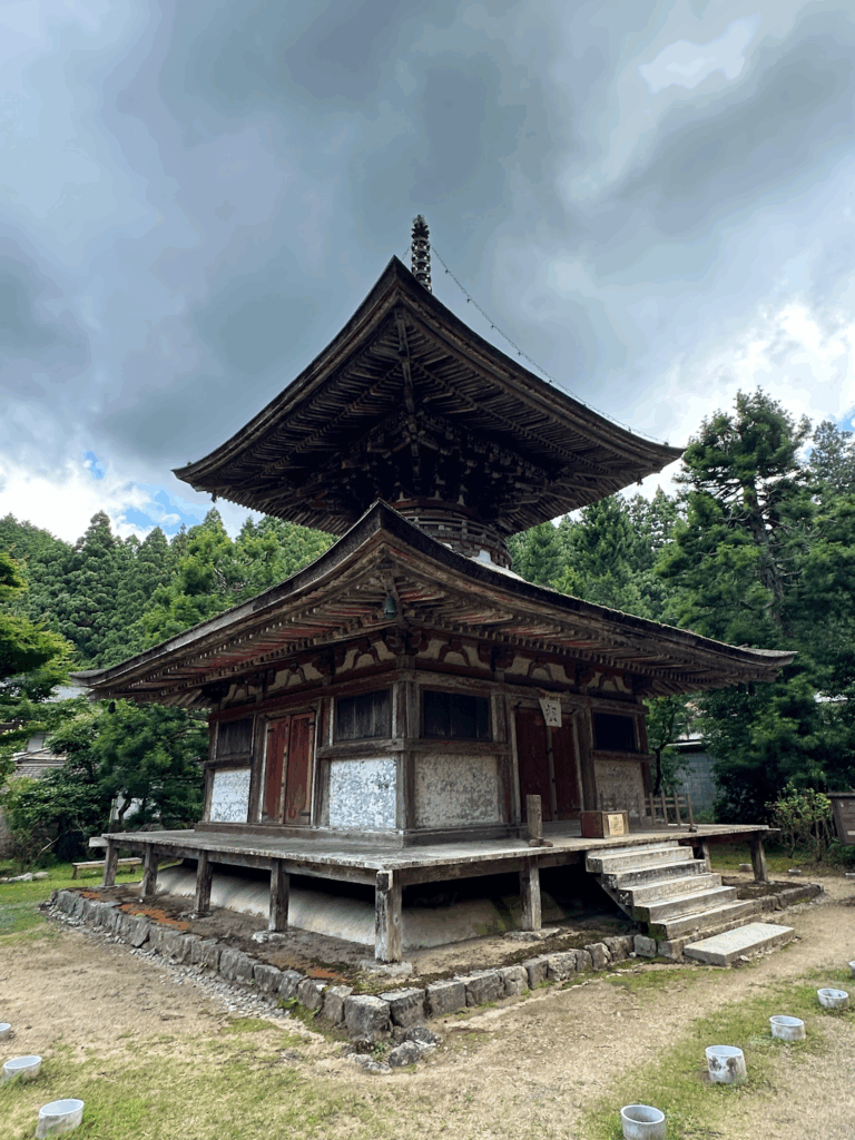 高野山金剛三昧院の古い木造の塔状建築。風化した壁と精巧な屋根の造りが特徴で、木々に囲まれている。