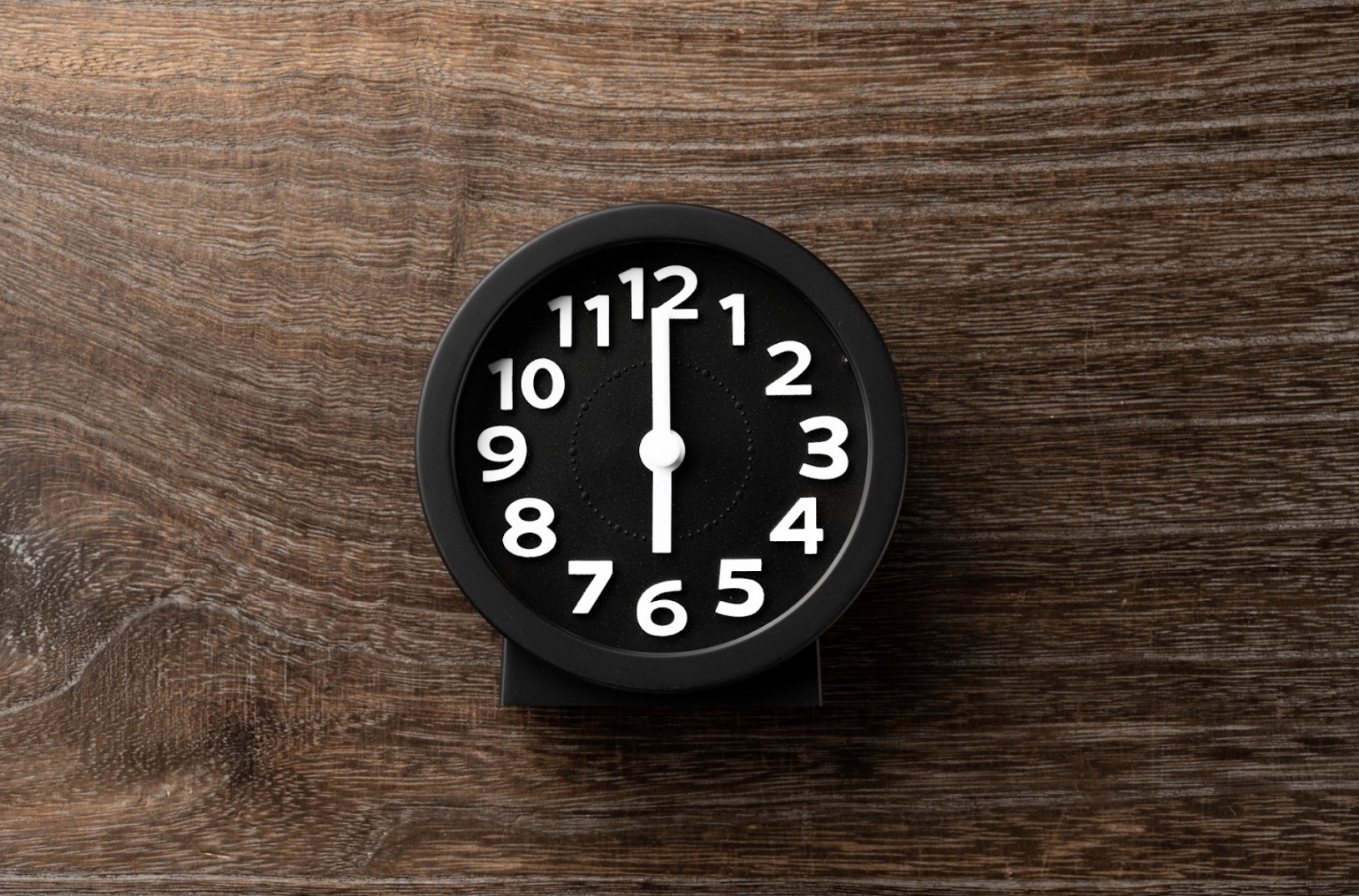 A black clock placed on a wooden table, with the hands pointing exactly at 12 o'clock: Meditation Timer