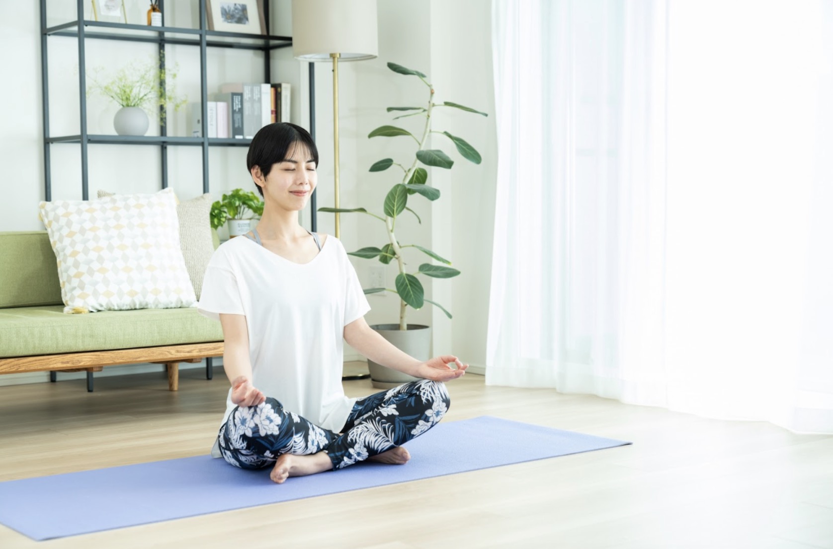明るいリビングでヨガマットの上に座り、目を閉じて瞑想する女性。穏やかな表情でリラックスしている：10分間の瞑想
