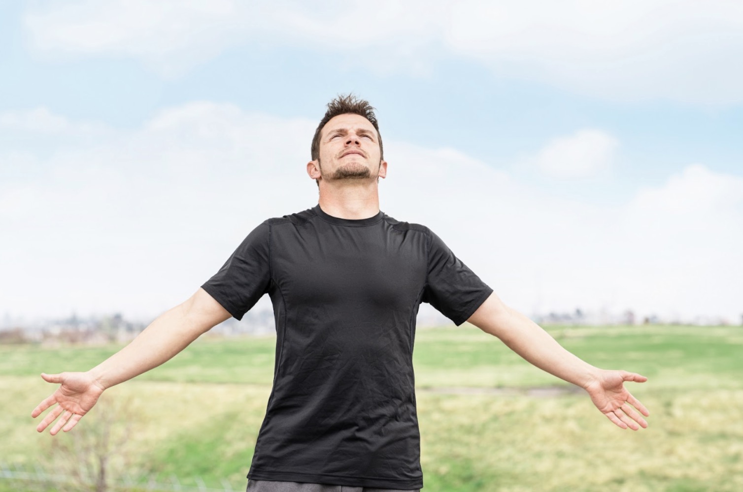 Man standing under the blue sky with arms outstretched, taking a deep breath :Breathing Exercise for Nerves