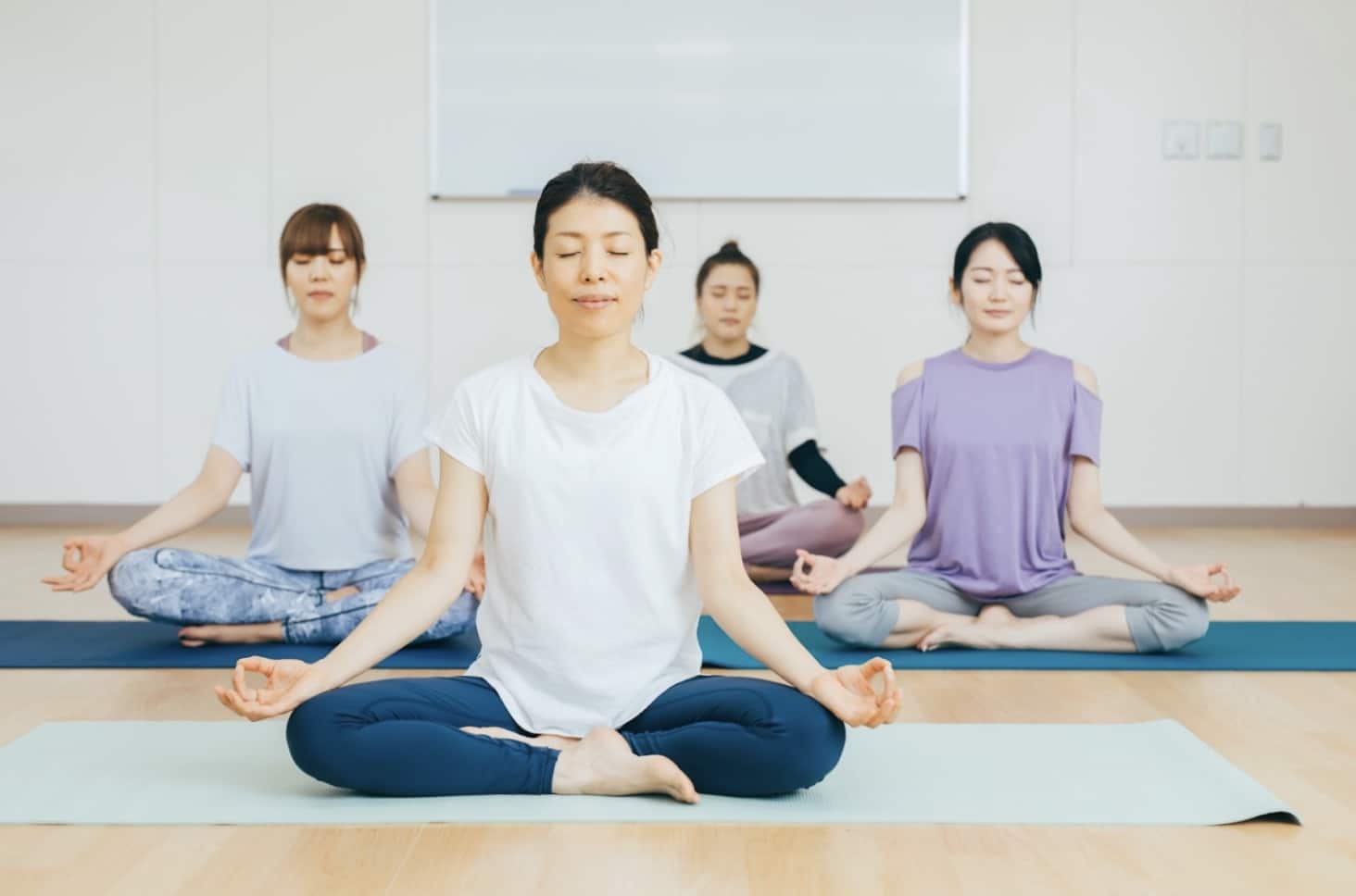 Four women sitting on yoga mats in meditation. They all have their eyes closed and calm expressions, depicting a scene from a meditation or yoga class :Meditation Center