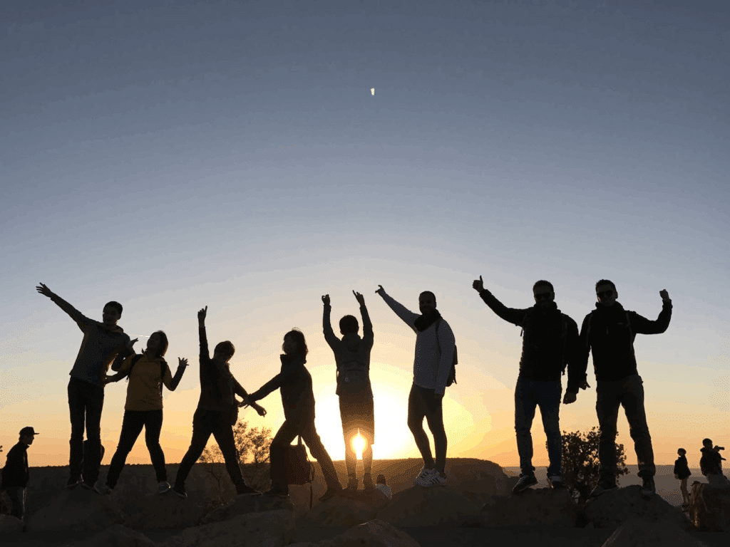 A group of people standing on rocks, striking poses in silhouette against the sunset. A joyful scene capturing friends on a trip :Meditation Center