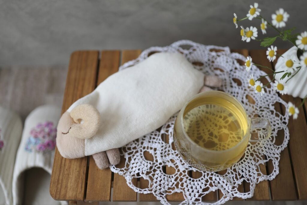 A plush sheep, a glass cup of chamomile tea, and a white lace doily on a wooden table, creating a calm and relaxing atmosphere : How to Relax Anywhere