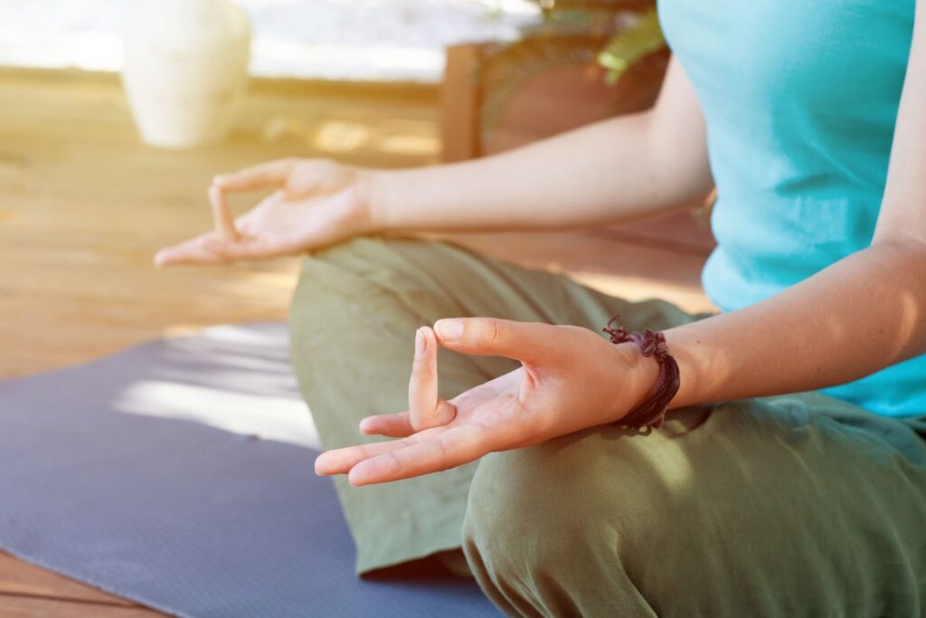 Close-up of a person meditating on a yoga mat, sitting cross-legged with hands resting on the knees in a mudra gesture, conveying a calm and relaxed atmosphere : How to Relax Anywhere