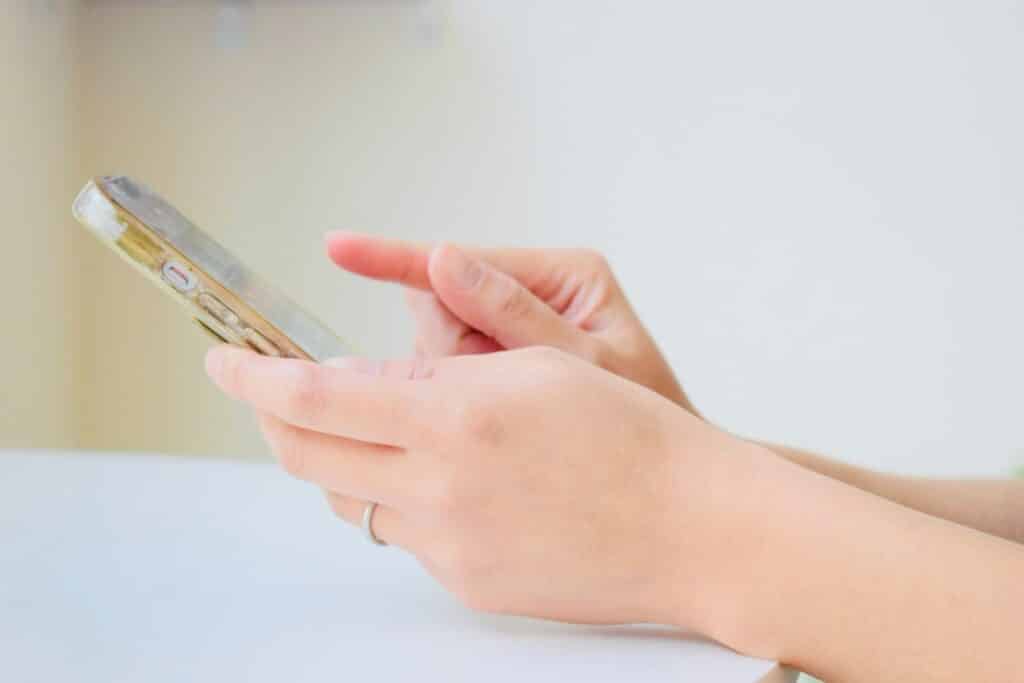 スマートフォンを手に取り、指で画面を操作している様子のクローズアップ。明るい背景の中で、集中してスマホを使っている:ガイド付き筋弛緩法