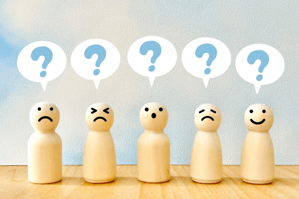 Wooden dolls with different facial expressions (angry, sad, surprised, happy, etc.) lined up, each with a speech bubble showing a question mark above their heads, symbolizing emotions and moods :Meditation Center