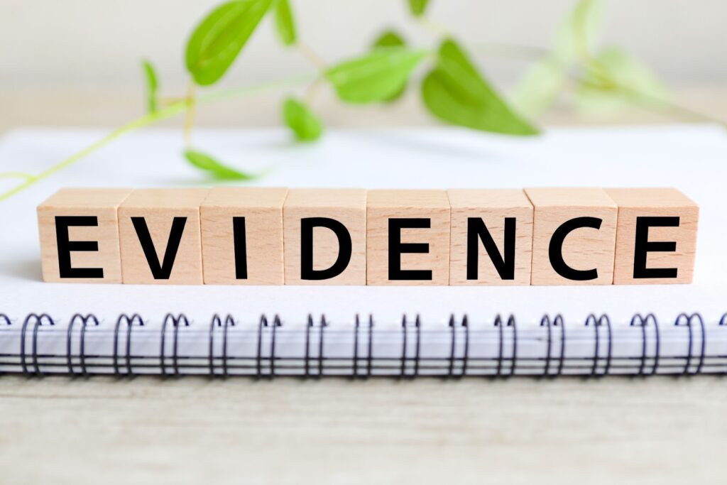 ノートの上に木製のブロックが並び、「EVIDENCE(証拠)」という文字が黒字で書かれている。背景には緑の植物があり、明るくナチュラルな雰囲気:ガイド付き筋弛緩法