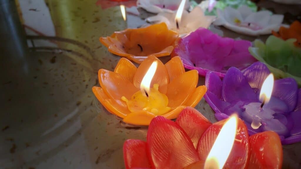 水面に浮かぶ色とりどりの花形キャンドルが静かに灯り、柔らかな光が穏やかに反射している。オレンジ、赤、紫、白などのキャンドルが瞑想や祈りの雰囲気を演出している：Matter Over Mind