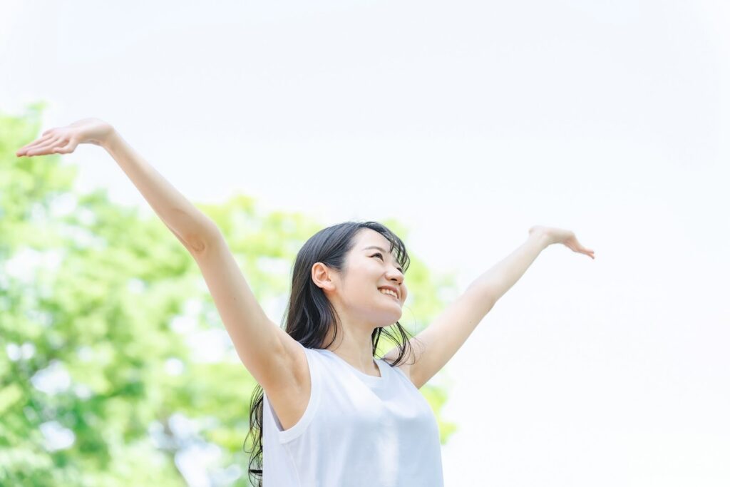 青空の下で両手を広げ、笑顔で深呼吸する女性。爽やかな朝のエネルギーを感じている：10分間の瞑想