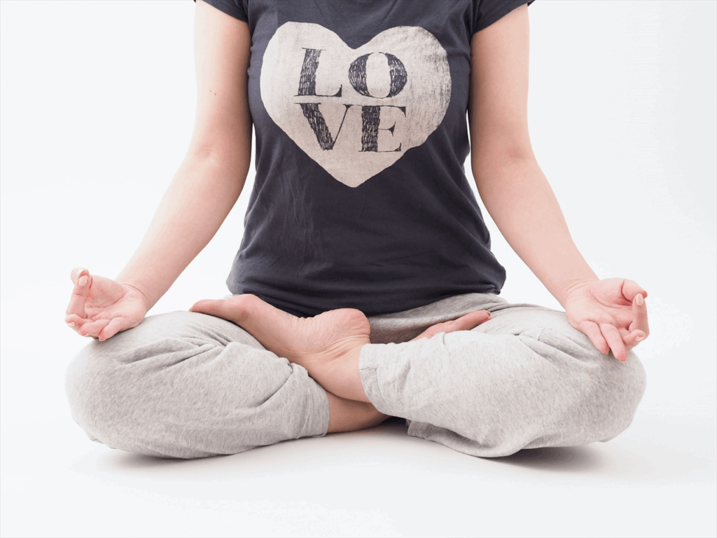 A person wearing a T-shirt with the word “LOVE” sits cross-legged on the floor, hands resting on their knees in a meditation pose, exuding a calm and relaxed atmosphere. :Meditation Positions