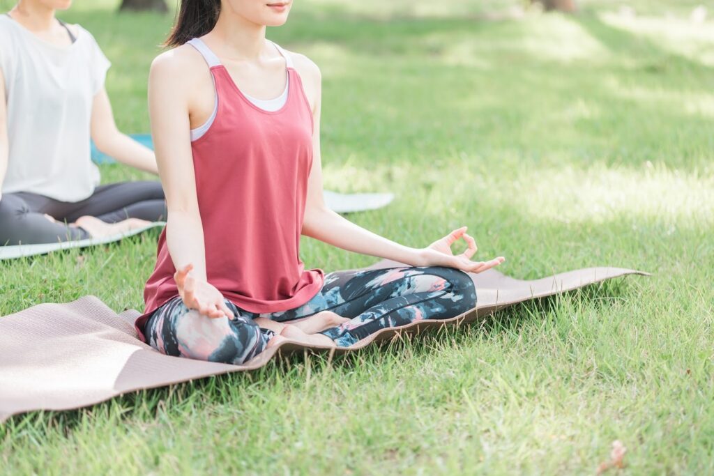 A woman sits cross-legged on a yoga mat on the grass, meditating peacefully under gentle sunlight: Meditation Technique