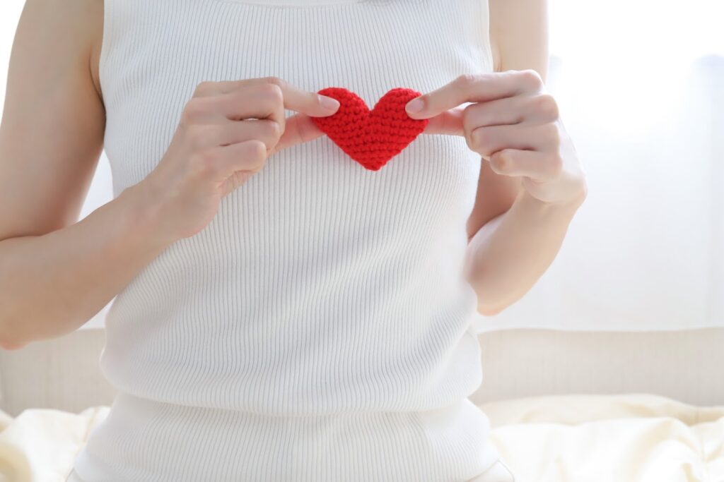 A woman in a white sleeveless top gently holds a red knitted heart in front of her chest, symbolizing self-love, emotional care, and kindness: Meditation for Beginners