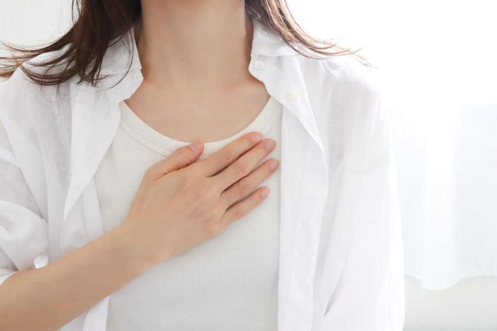 A woman in white clothing placing her hand over her chest, symbolizing calmness, mindfulness, and self-awareness in a gentle light: MBSR