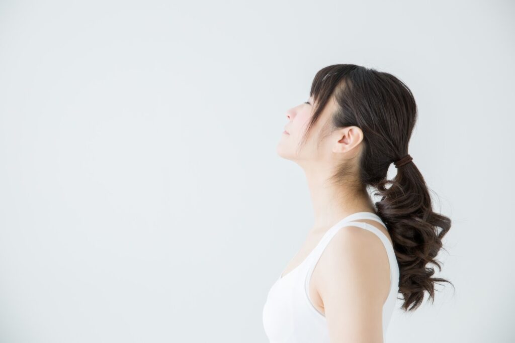 白い背景の前で静かに上を見上げる女性。穏やかな表情で呼吸を整えるように立ち、心の落ち着きやマインドフルネスを感じさせるイメージ：TM瞑想
