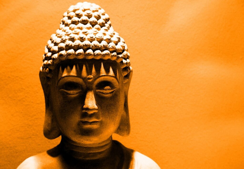 金色の照明に照らされた仏像のクローズアップ。穏やかな表情を浮かべた顔が柔らかな陰影に包まれ、神聖で静謐な雰囲気を醸し出している：TM瞑想