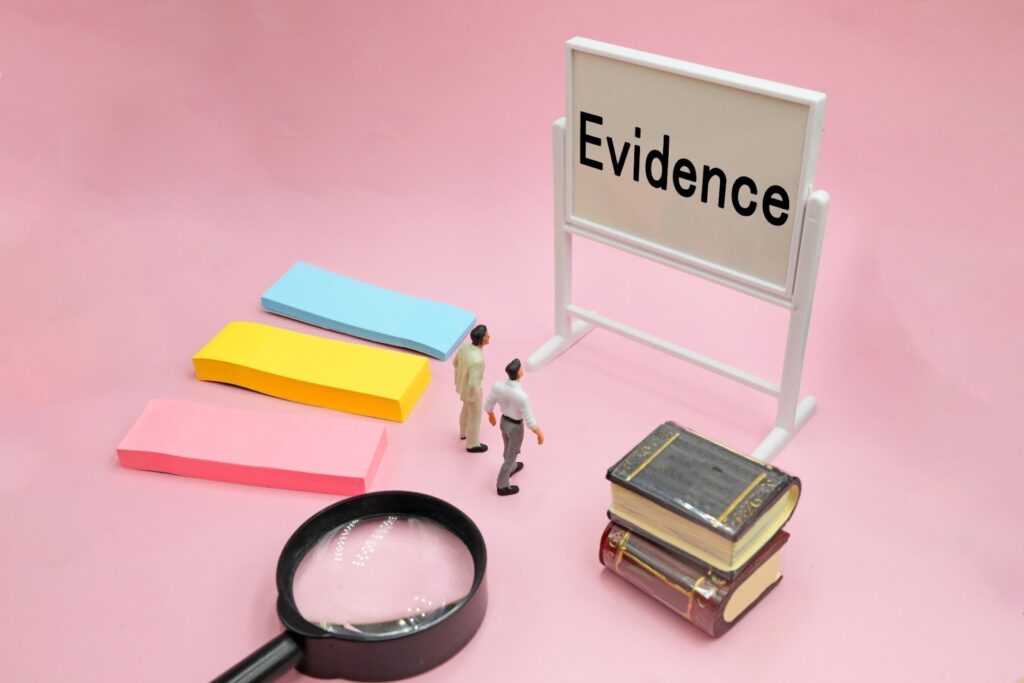 A conceptual image with a pink background featuring a board labeled “Evidence,” a magnifying glass, sticky notes, stacked books, and two miniature figures observing the scene, symbolizing research and investigation: Mindfulness Techniques