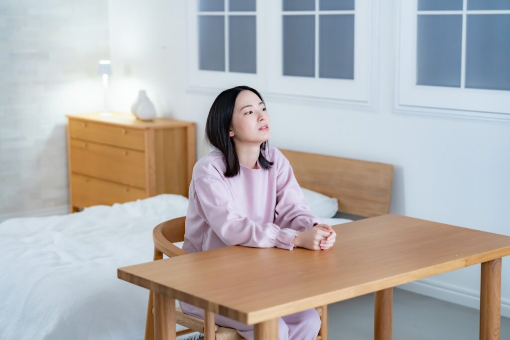 A woman in pajamas sitting at a wooden table in a bedroom, appearing thoughtful or pensive — conveying a calm and reflective evening mood: Mindfulness Journal
