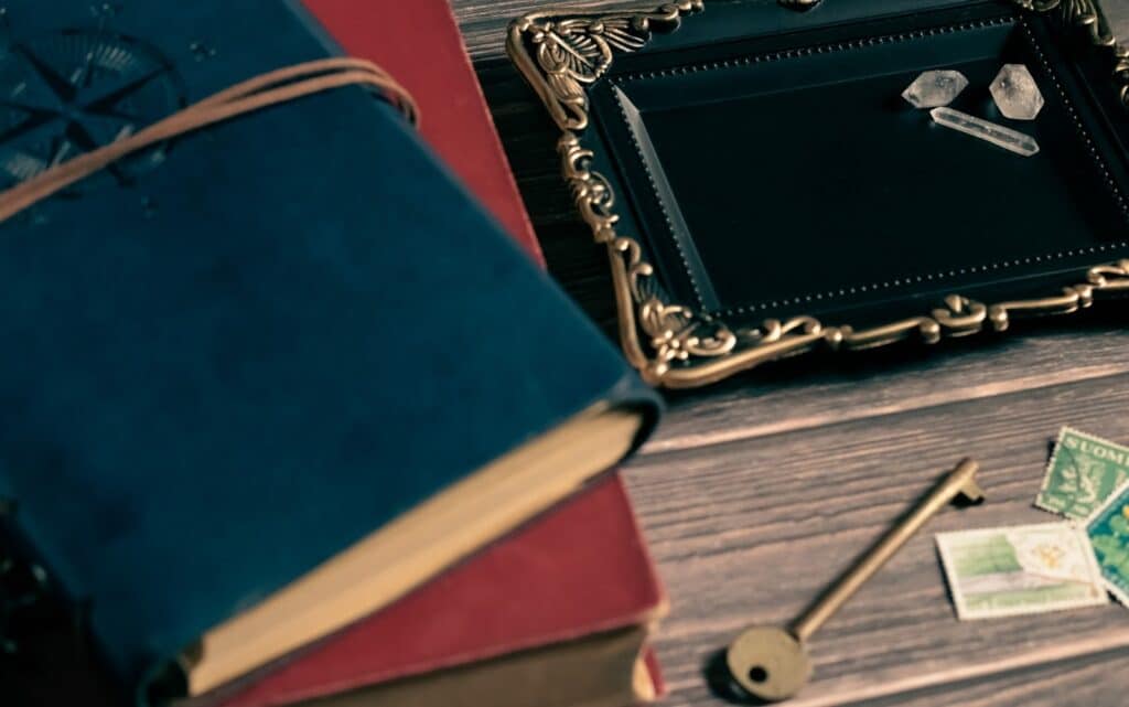 Vintage-style desk with blue and red journals, an ornate picture frame, an old brass key, postage stamps, and clear quartz crystals — evoking a mysterious and nostalgic atmosphere: Mindfulness Journal