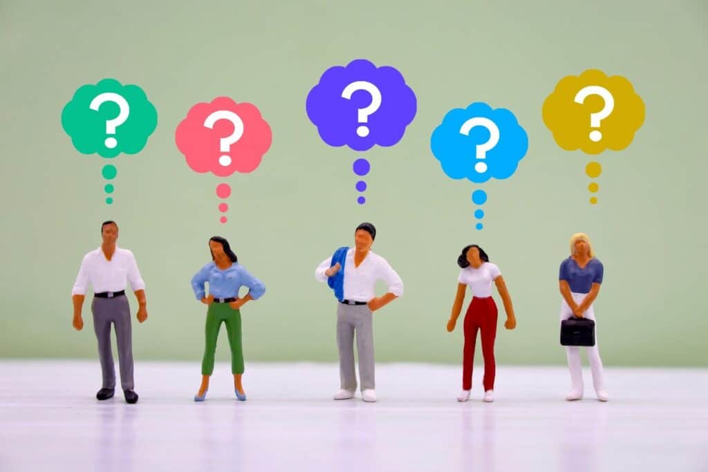 Five miniature figurines stand in a row, each with a colorful thought bubble containing a question mark above their head — symbolizing curiosity or confusion: Mindfulness Journal