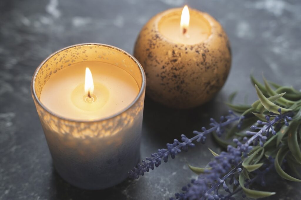 テーブルの上に置かれた2つのアロマキャンドルが優しく灯り、そばにはラベンダーの花が添えられている。穏やかでリラックスした雰囲気を感じる光景：スピリチュアル・プラクティス