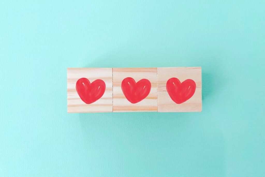Three wooden blocks lined up horizontally, each painted with a red heart on a soft mint green background — symbolizing love, kindness, and positivity: The Chimp Paradox