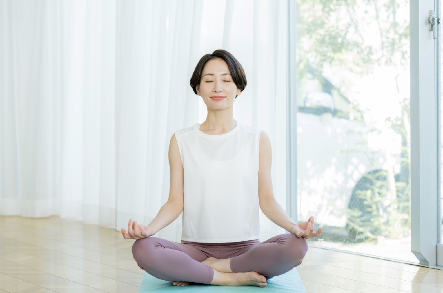 室内でヨガマットに座り、目を閉じて静かに瞑想する人物。柔らかな自然光が差し込む落ち着いた空間：毎日の瞑想