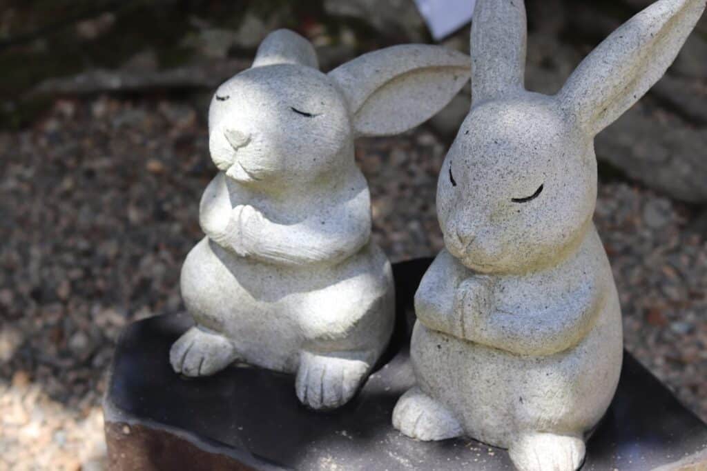 Two stone rabbit statues sitting with hands together in a prayer-like pose, featuring calm and serene expressions outdoors: Mindful Souls