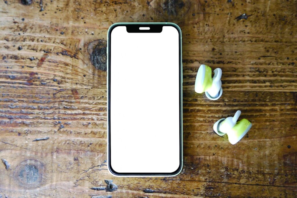 木製テーブルの上に、白い画面を表示したスマートフォンとワイヤレスイヤホンが置かれている:毎日の瞑想