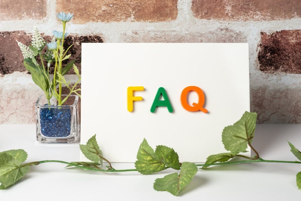 A white board with colorful letters spelling ‘FAQ’ placed on a table, with a small vase of artificial flowers and green leaves beside it: Meditation Groups