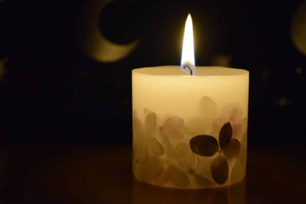 暗い背景の中で、装飾模様のあるキャンドルに小さな炎が灯っている。柔らかな光が周囲を静かに照らしている：睡眠瞑想