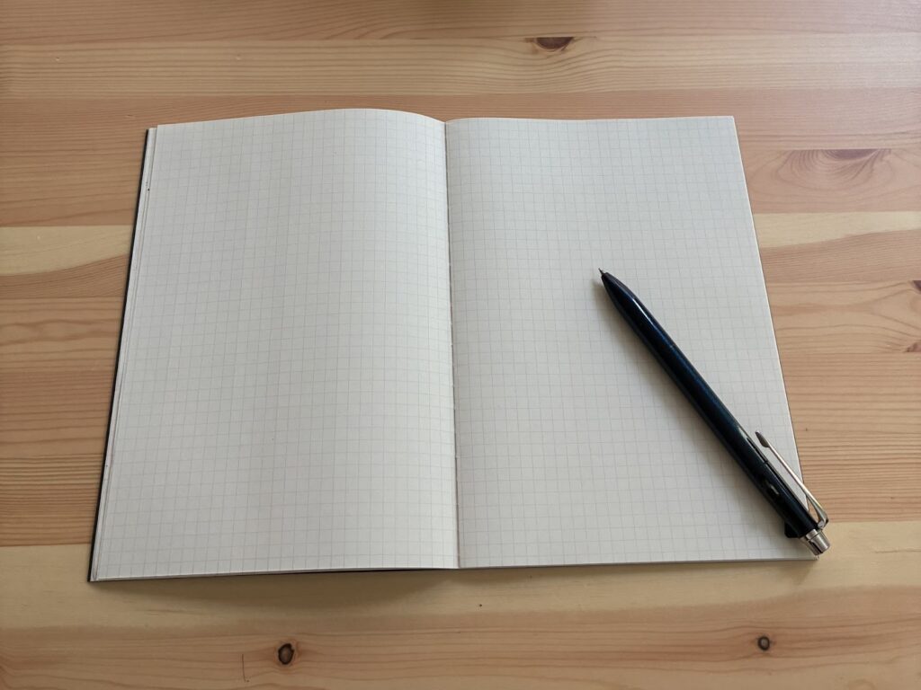 An open grid notebook lying on a wooden desk, with a black pen placed on the right-hand page: Mind Over Mood