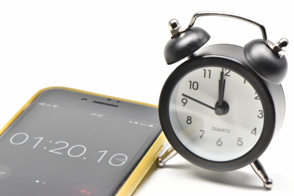 Close-up of a smartphone meditation timer next to a black analog alarm clock on a white background.